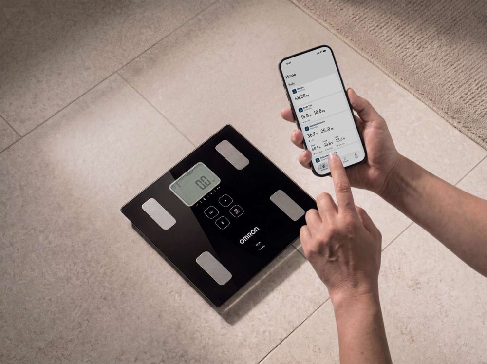 Omron VIVA på gulvet med OMRON connect-appen på en telefon